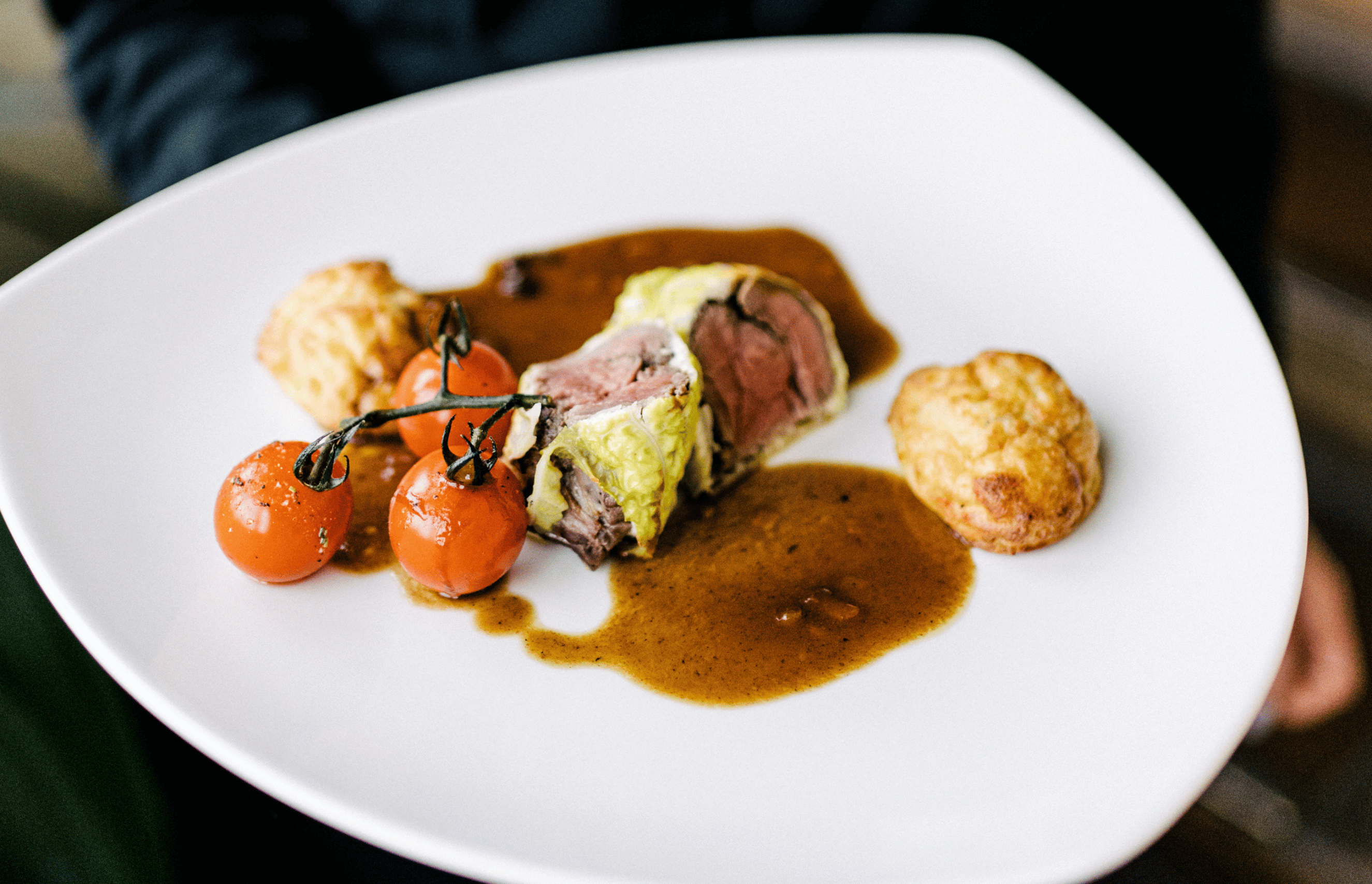 Ein angerichteter Teller mit Ente, Sauce, Kartoffelgebäck und Tomaten