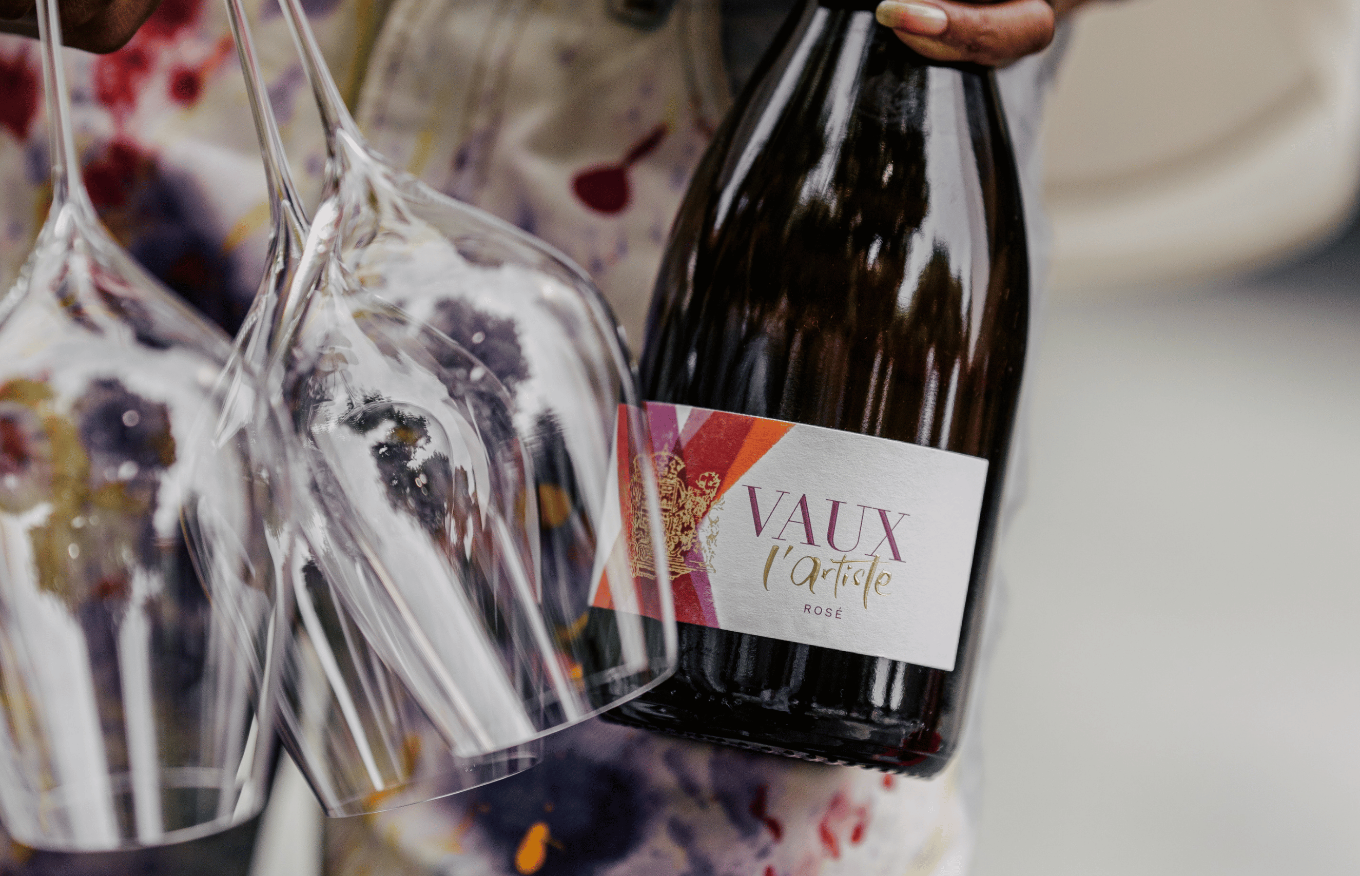 Frau hält seine Flasche l´Artiste Rosé und zwei leere Gläser Sekt in der Hand